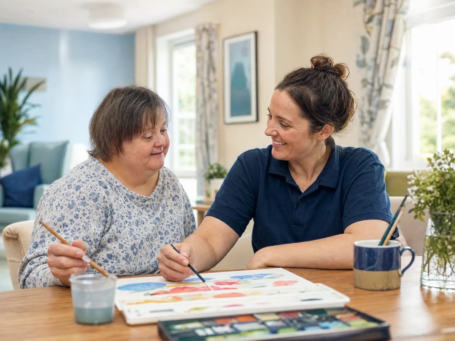 Care professional and adult service user painting together at a table.